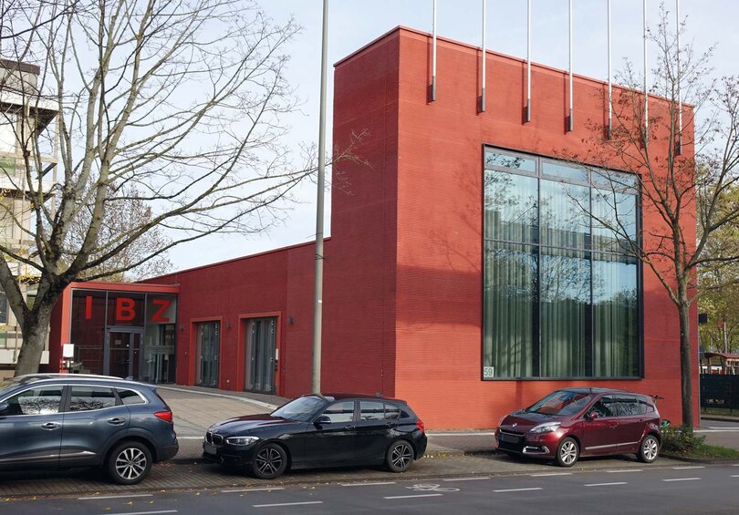 Das Bild zeigt einen markanten roten Bau, in dem das Internationale Begegnungszentrum (IBZ) der TU Dortmund untergebracht ist; es grenzt unmittelbar an das Gebäude der Zentralen Studienberatung.