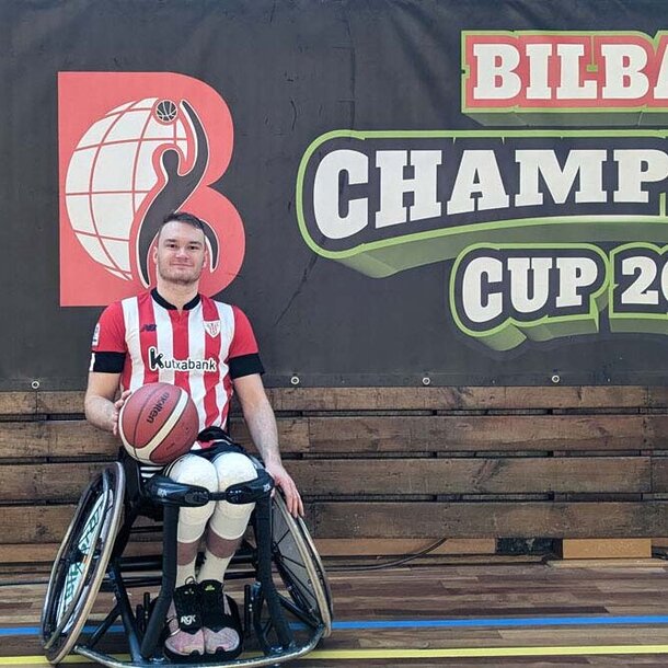 Bild von Lukas Gloßner als Rollstuhlbasketballer im Trikot der BIDAIDEAK BILBAO BSR und in seinem speziellen Sport-Rollstuhl vor einem Werbebanner in einer  Basketballhalle