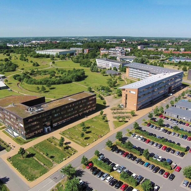 Luftbildperspektive auf den Campus der Europa-Uni Flensburg mit Parkplätzen, Gebäuden und weitläufigen Grünflächen